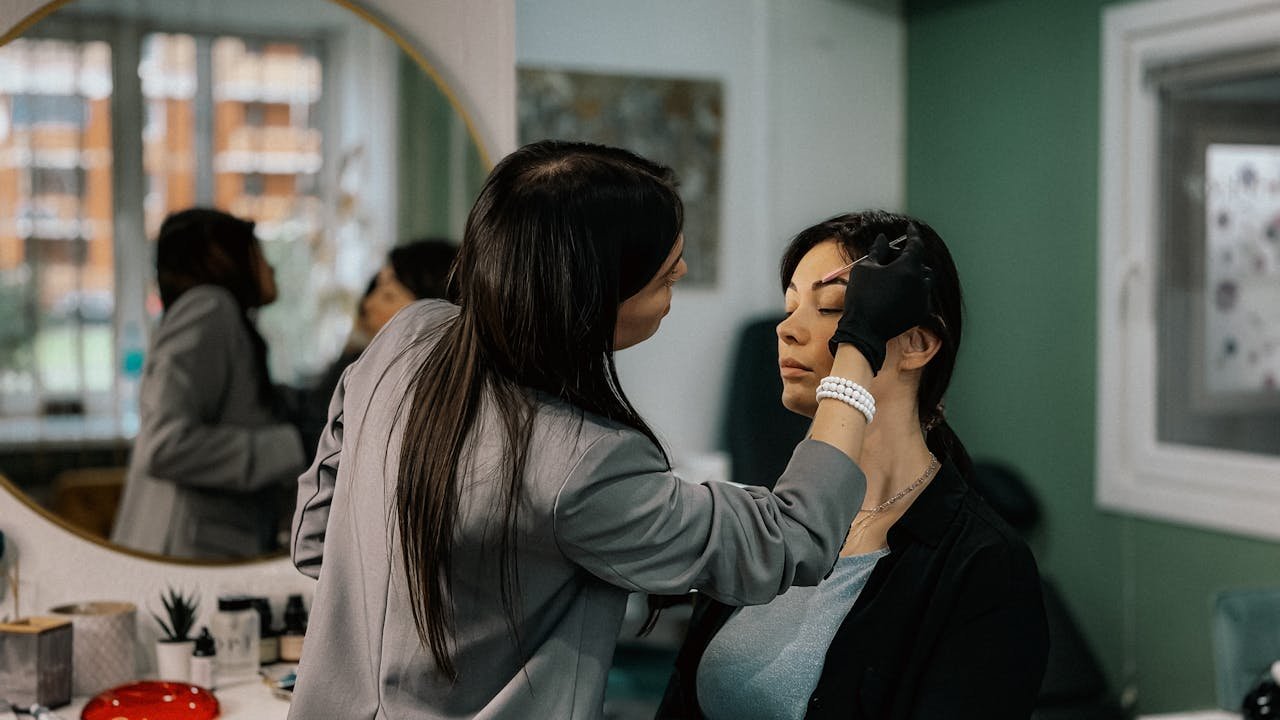 Services A makeup artist professionally applies eyebrow makeup to a female client in a salon.
